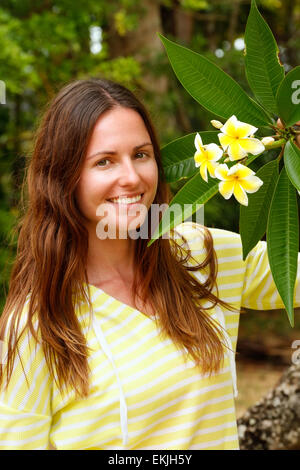 Junge Frau, die durch gelbe Plumeria Baum Stockfoto