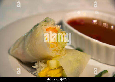 Stücke von Mango und Shrimps sind in Sommer-Rollen in Soße getunkt werden gefaltet. Stockfoto