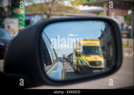 Ein Rennsport-Krankenwagen mit Blaulicht überholt ein Auto, das es in seiner Flügel Spiegel sieht Stockfoto