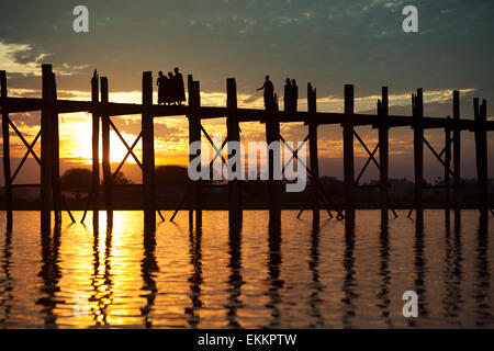 Silhouettenhafte Figuren (buddhistische Mönche und lokal gekleideten Frauen) auf die U Bein Brücke über Taungthaman See bei Sonnenuntergang. Stockfoto