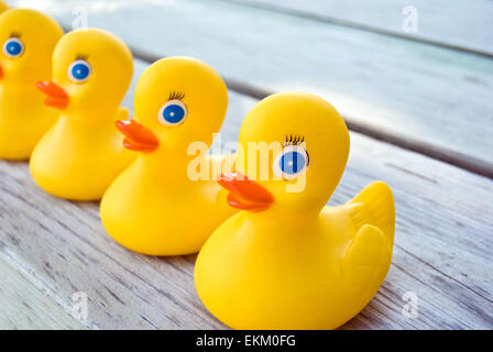 Gelbe Gummienten in einer Reihe auf verwittertem Holz. Stockfoto