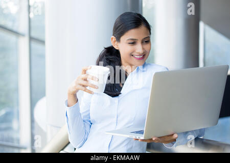 Closeup, Porträt, junge, attraktive Frau stehen, Kaffeetrinken, lächelnd auf der Suche, den silbernen Laptop surfen. Stockfoto