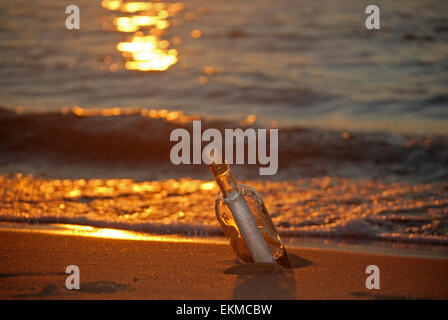 Eine Flaschenpost bei Sonnenuntergang am Strand. Stockfoto