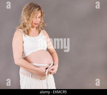 eine junge blonde Frau, die ihren Bauch mit einem Maßband messen Stockfoto