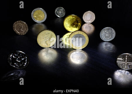 Münzen aus verschiedenen Währungen auf eine schwarze Fläche reflektiert. Stockfoto