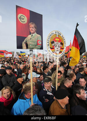 Unterstützer der deutschen Anti-Islam Organisation Pegida (Patriotischen Europäer gegen die Islamisierung des Abendlandes) tragen ein Zeichen, das liest "Stasi Nationalagentur" und eine Anzeige ein Bild von Merkel in einer einheitlichen erinnert an eine SS-Uniform gekleidet, wie sie durch Dresden, Germany, 13. April 2015 Rallye. Statt ein Hakenkreuz zeigt das Bild eine Euro-Zeichen auf der Brassard um Merkels Arm. Pegida eingeladen, niederländischer Rechtspopulist Wilders, während ihrer Demonstration zu sprechen. Foto: Jan Woitas/dpa Stockfoto