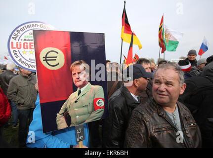 Unterstützer der deutschen Anti-Islam Organisation Pegida (Patriotischen Europäer gegen die Islamisierung des Abendlandes) tragen ein Schild liest "Quality Seal Pack von Lügnern für alle Beteiligten" und eine Anzeige ein Bild von Merkel in einer einheitlichen erinnert an eine SS-Uniform gekleidet, wie sie durch Dresden, Germany, 13. April 2015 Rallye. Statt ein Hakenkreuz zeigt das Bild eine Euro-Zeichen auf der Brassard um Merkels Arm. Pegida eingeladen, niederländischer Rechtspopulist Wilders, während ihrer Demonstration zu sprechen. Foto: Jan Woitas/dpa Stockfoto