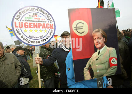 Unterstützer der deutschen Anti-Islam Organisation Pegida (Patriotischen Europäer gegen die Islamisierung des Abendlandes) tragen ein Schild liest "Quality Seal Pack von Lügnern für alle Beteiligten" und eine Anzeige ein Bild von Merkel in einer einheitlichen erinnert an eine SS-Uniform gekleidet, wie sie durch Dresden, Germany, 13. April 2015 Rallye. Statt ein Hakenkreuz zeigt das Bild eine Euro-Zeichen auf der Brassard um Merkels Arm. Pegida eingeladen, niederländischer Rechtspopulist Wilders, während ihrer Demonstration zu sprechen. Foto: Jan Woitas/dpa Stockfoto