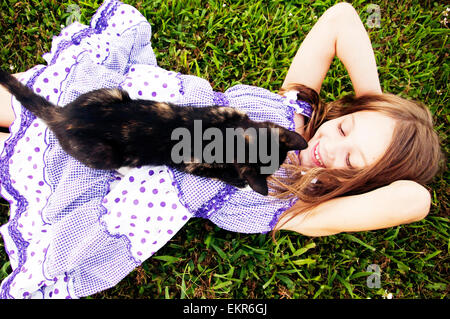 Mädchen auf dem Rasen mit schwarzem Calico Katze liegend Stockfoto