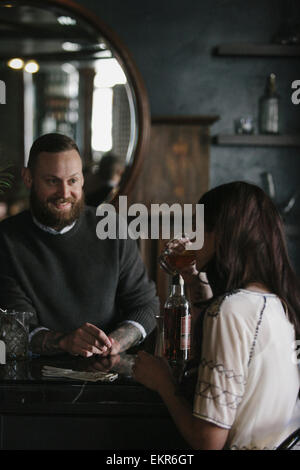 Eine Frau und ein Barkeeper sprechen, und Getränke mischen. Stockfoto