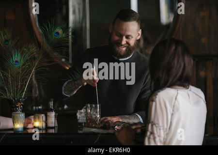 Eine Frau und ein Barkeeper sprechen, und Getränke mischen. Stockfoto