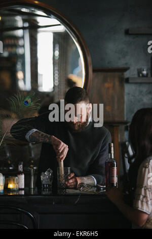 Eine Frau und ein Barkeeper sprechen, und Getränke mischen. Stockfoto