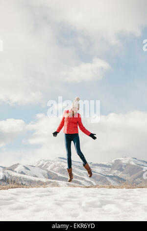 Ein junges Mädchen mit langen Beinen und rote Jacke, springen in die Luft über dem Schnee Stockfoto