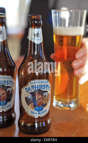 Flaschen und ein mans Hand heben ein Glas Dr Thirsty blondes Bier von Wychwood Brewery Stockfoto