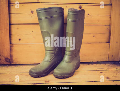 Ein paar Gummistiefel (gumboots) auf einem Holzboden vor einer Holztür. Stockfoto