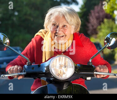 Nahaufnahme einer älteren Frau Beschleunigung auf einem Scooter Bike mitten auf der Straße ohne Helm. Stockfoto