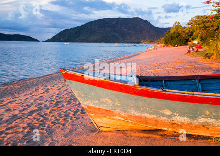 Ein Boot an einem Strand in Cape Maclear am Ufer des Lake Malawi, Malawi, Afrika, bei Sonnenuntergang. Stockfoto