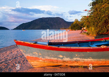 Ein Boot an einem Strand in Cape Maclear am Ufer des Lake Malawi, Malawi, Afrika, bei Sonnenuntergang. Stockfoto