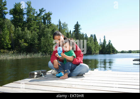 Native Aboriginal Mutter auf ein Dock mit ihrem Sohn In Untiefe See, Ontario, Kanada. Stockfoto