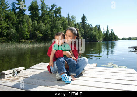 Native Aboriginal Mutter auf ein Dock mit ihrem Sohn In Untiefe See, Ontario, Kanada. Stockfoto