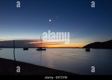 Sonnenuntergang am Cape Maclear am Ufer des Lake Malawi Blick auf Berge auf dem jenseitigen Ufer mit einem Mond, Planeten und Sternen, Stockfoto