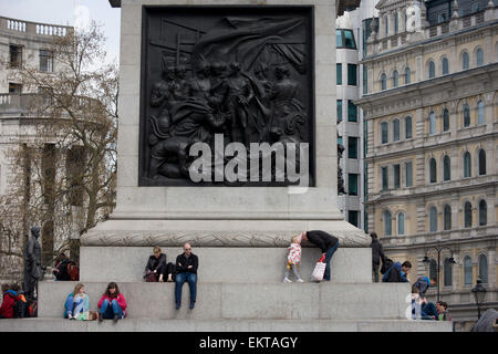 Touristen sitzen unter der Schlacht von Kap St. Vincent von Musgrave Watson und William F. Woodington, das Relief an der Westwand des Sockels auf Nelson Säule auf dem Trafalgar Square. Stockfoto
