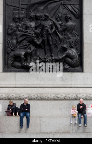 Touristen sitzen unter der Schlacht von Kap St. Vincent von Musgrave Watson und William F. Woodington, das Relief an der Westwand des Sockels auf Nelson Säule auf dem Trafalgar Square. Stockfoto