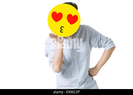 Junger Mann mit einem romantischen Emoticon Gesicht vor seinem Gesicht Stockfoto