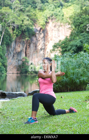 Sportliche Frau dehnen Trizeps Rückseite Arms dabei Longe in einem Outdoor-Park. Stockfoto