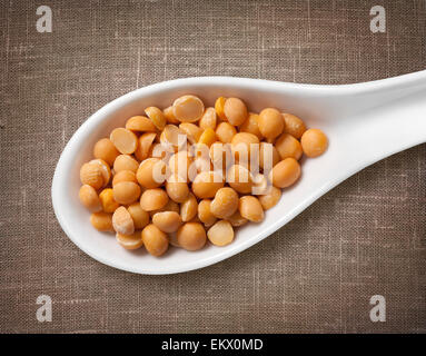Gelbe Erbsen in weißem Porzellanlöffel / Highres Foto von Korn in weißem Porzellan Löffel auf Jute Sackleinen Hintergrund Stockfoto