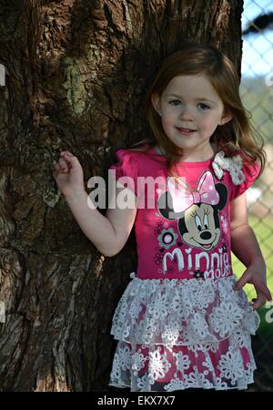 Ziemlich vier Jahre altes Mädchen in rosa posieren durch einen Baum. Stockfoto