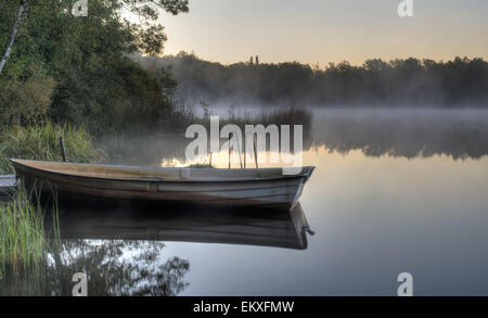 Ein Ruderboot mit einem Pier an einem ruhigen schwedischen See mit Nebel über. Es ist früh am Morgen und alles ist still. Stockfoto