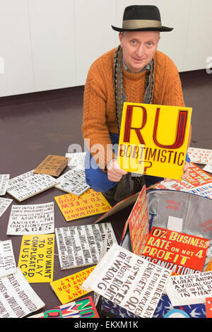 London, UK. 13. April 2015. Künstler Bob und Roberta Smith (orange Jumper) hält ein RU Bobtimistic Schild an der Cass, London Metropolitan University. Mehr als drei Wochen im Vorfeld der Parlamentswahlen als Künstler Bob und Roberta Smith (Patrick Brill) gegen Michael Gove im Surrey Heath Wahlkreis stehen wird Smith/Brill Studenten und Aktivisten The Arts Notrufzentrale in der Cass Bank Gallery in einem indoor Protest gegen Mittelkürzungen Kunst führen. Foto: Bettina Strenske Stockfoto