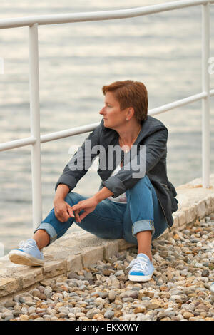 Applying kaukasischen gebräunte Frau im Herbst Kleidung sitzt auf dem felsigen Strand Stockfoto