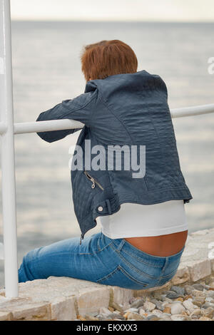 Applying kaukasischen gebräunte Frau im Herbst Kleidung sitzt auf dem felsigen Strand Stockfoto