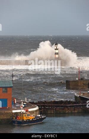 Seaham, Teesside, England; Wellen, die in einem Leuchtturm und ein Boot am Pier entlang Stockfoto