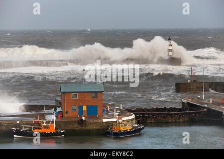 Seaham, Teesside, England; Wellen, die in einem Leuchtturm und Boote auf einem Pier Stockfoto