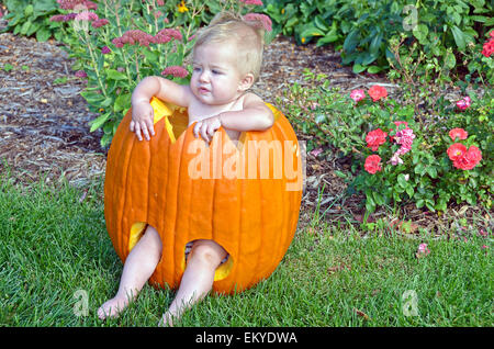 Kleine blonde Mädchen sitzen in einem Halloween geschnitzten Kürbis. Stockfoto