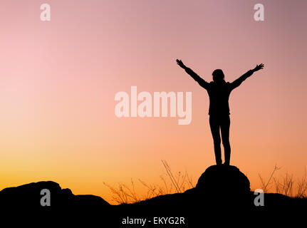 Silhouette der glückliche junge Frau mit gegen schönen bunten Himmel erhobenen Armen. Sommer Sonnenuntergang. Landschaft Stockfoto