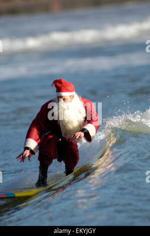 Santa Claus geht surfen und Fänge eine Welle auf einem gelben Surf Board Stockfoto
