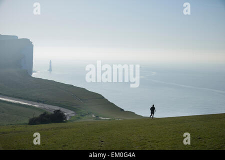 Durch einen frühen Morgennebel, ​ Beachy Head Lighthouse gesehen werden kann wie ein Mann an der Spitze der Klippen an Birling Gap in East Sussex, England. Stockfoto