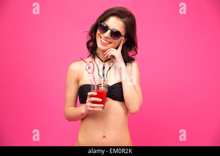 Stets gut gelaunte Frau im Badeanzug mit frischen Saft über rosa Hintergrund Stockfoto