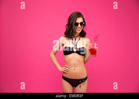 Lächelnde junge Frau in Badeanzug und eine Sonnenbrille mit Glas frischen Saft Stockfoto