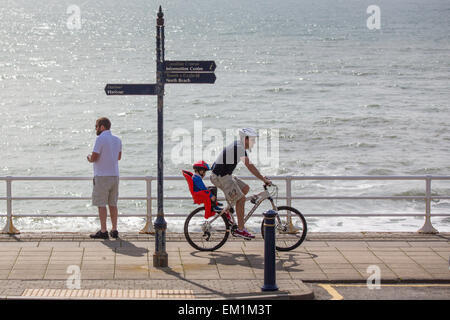 Aberystwyth, Wales, UK. 15. April 2015.  Das Wetter. Ein Radfahrer mit Kind und ein Mann auf Aberystwyth Promenade in der Frühlingssonne. Bildnachweis: Alan Hale/Alamy Live-Nachrichten Stockfoto