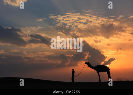 Silhouette Person mit einem Kamel bei Sonnenuntergang, Thar-Wüste in der Nähe von Jaisalmer, Rajasthan, Indien Stockfoto