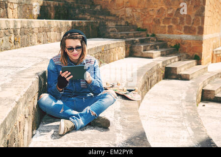 Freelancer-Kerl mit Dreadlocks auf Treppe sitzend mit digital-Tablette eingeben warm Nachrichtenfilter angewendet Stockfoto