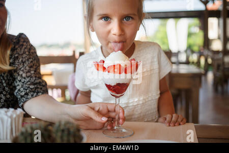 Kleines Mädchen Eis mit Erdbeeren in einem Restaurant Essen. Probieren Sie die Sprache in die Kamera schauen. Geringe Schärfentiefe f Stockfoto