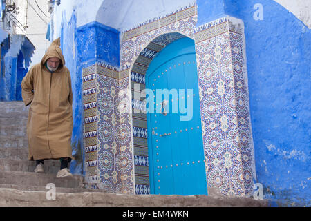 Berber Mann gekleidet in die typische Kleidung, die zu Fuß in der Nähe von einer blauen Tür in Chefchaouen (Chaouen), Rif-Gebirge, Marokko, Afrika Stockfoto