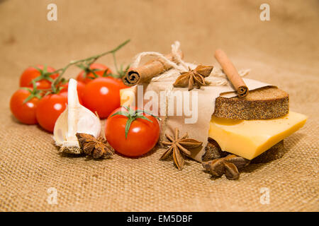Sandwich mit Käse eingewickelt in Papier, Zimtstange, Cherry-Tomaten und Knoblauch auf alten Tuch Stockfoto