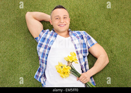 Hübscher junger Mann liegend auf dem grünen Rasen und hält einen Blumenstrauß Stockfoto